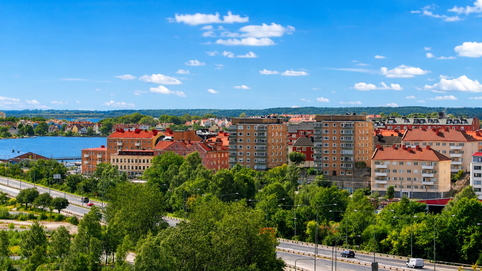 Pantarholmen district in Karlskrona, Sweden, with red-roofed apartment blocks, greenery and archipelago water beyond under a blue sky.