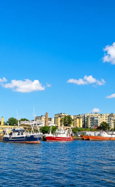 Saltö harbour in Karlskrona with fishing boats moored before waterfront apartment blocks under a bright blue sky