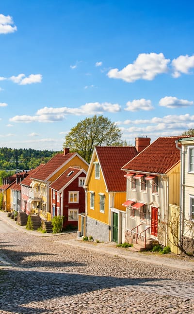 A steep cobbled Ronneby street lined with colourful traditional wooden houses under a blue sky with clouds.