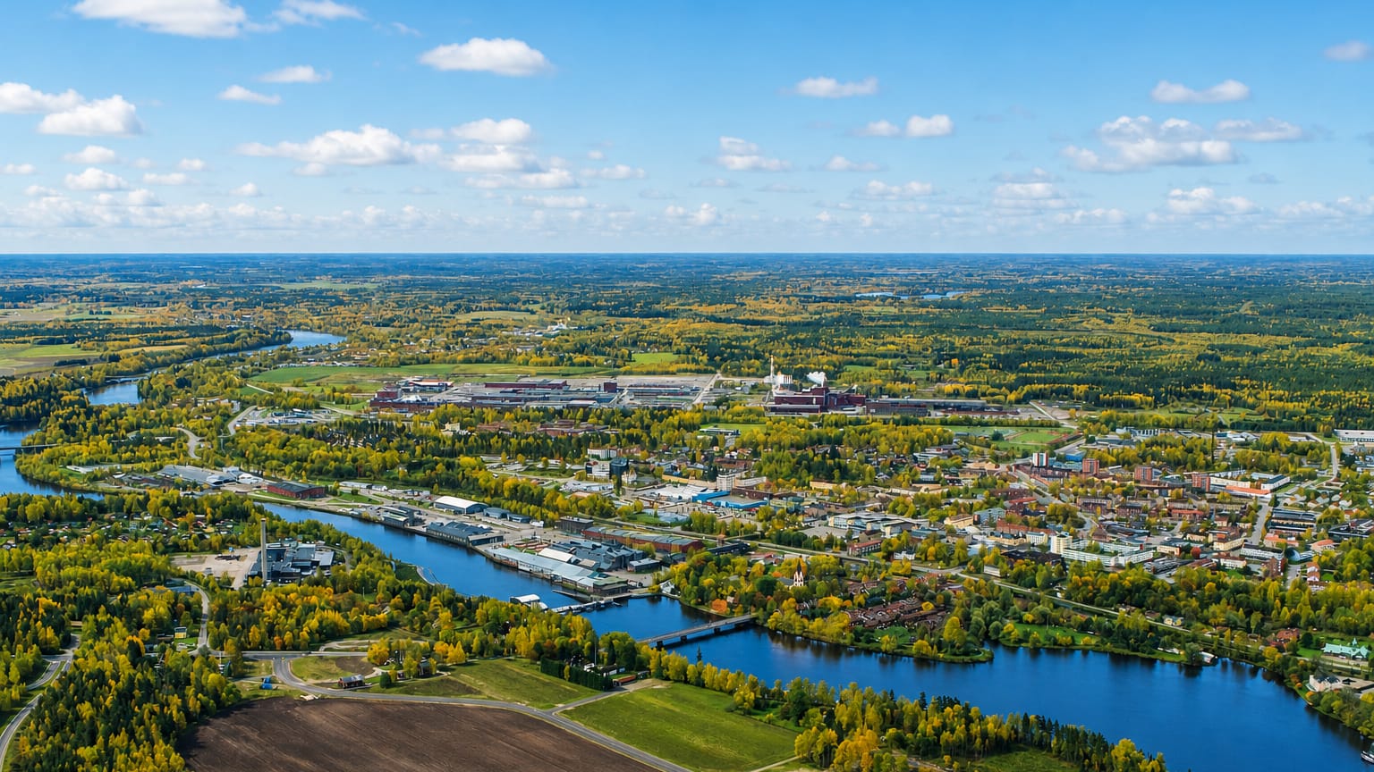 Wide aerial of Avesta, Sweden, stretching along a river through autumn-tinged forest