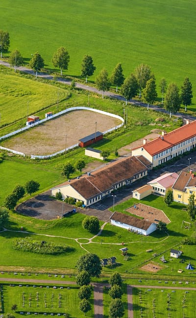 Aerial view of a red-roofed rural building complex among green fields and birch roads at Gagnef, Sweden.