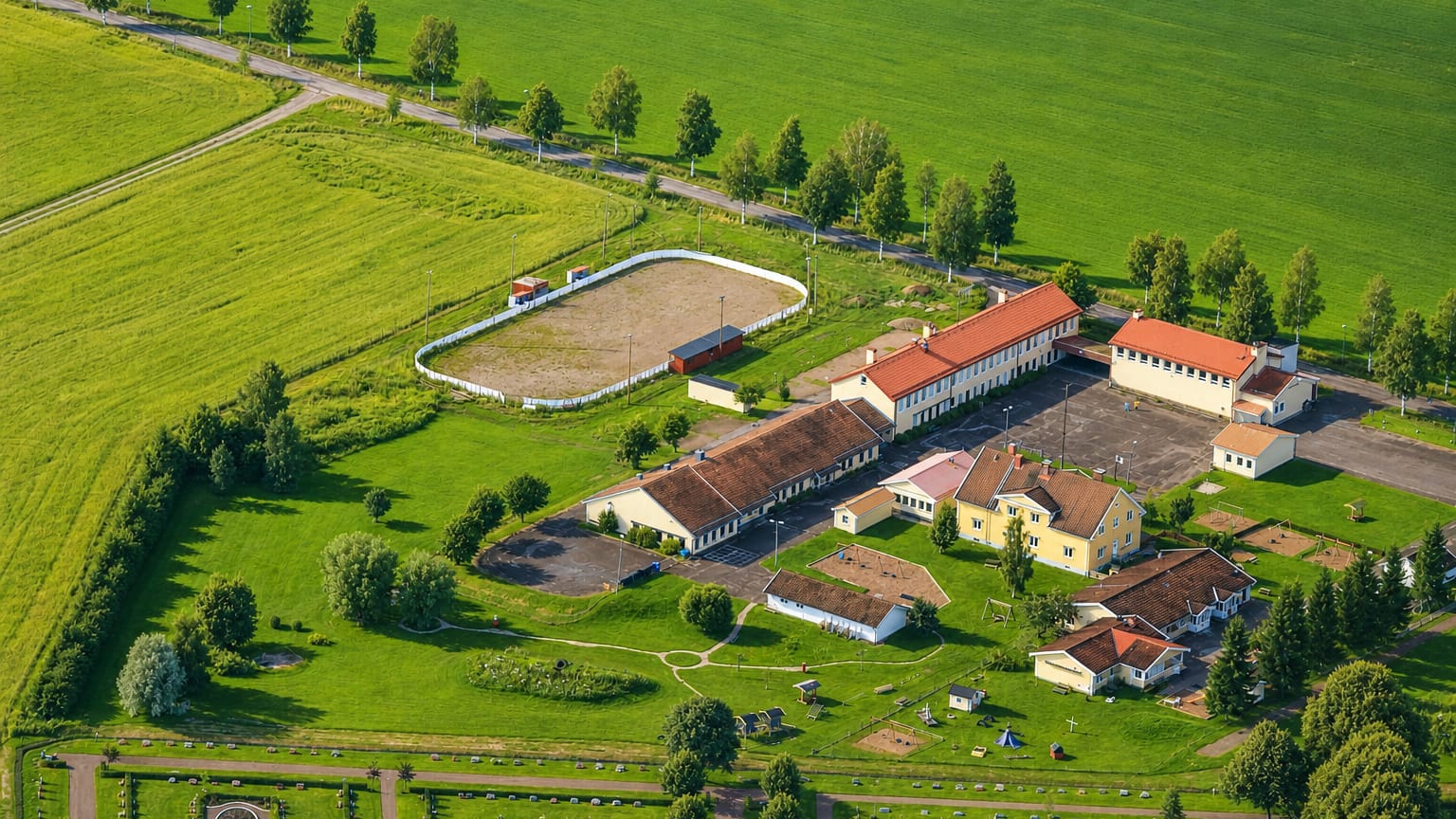 Aerial view of a red-roofed rural building complex among green fields and birch roads at Gagnef, Sweden.