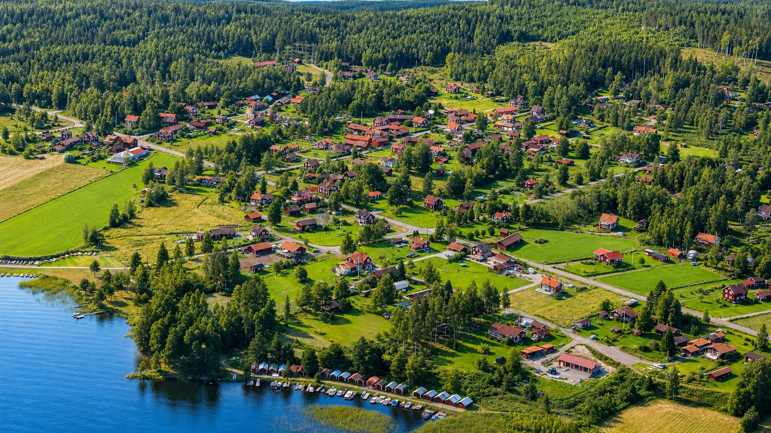 Aerial view of Leksand, Sweden, with Falu-red cottages, green fields and boat jetties along a forested lakeshore