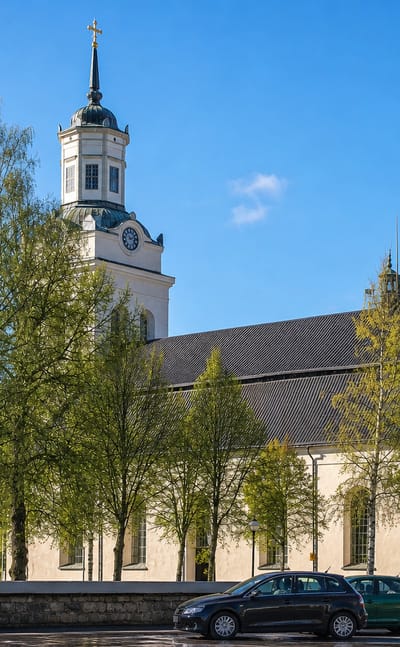 Orsa's large white church with its clock tower and cross flanked by spring birches under a blue sky.