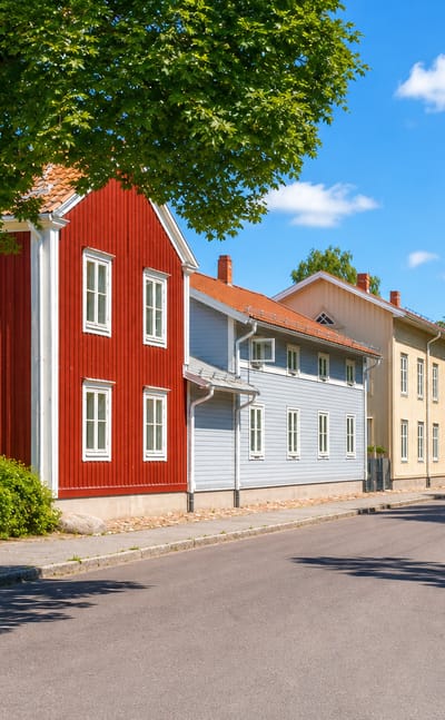 Sunlit street of red and pastel wooden houses in Smedjebacken, Dalarna, Sweden.