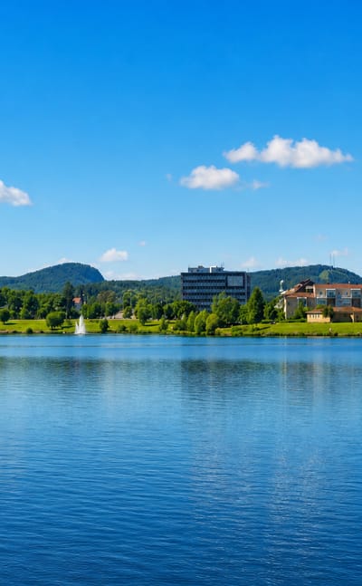 Bollnäs, Sweden, viewed across a calm lake, with a white church tower, a modern block and forested hills on the far shore.