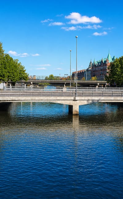 Canal and arched road bridge in Gavle, Sweden, with a moored boat and towered building beyond, under a blue sky