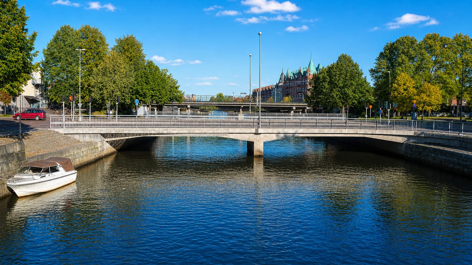 Canal and arched road bridge in Gavle, Sweden, with a moored boat and towered building beyond, under a blue sky