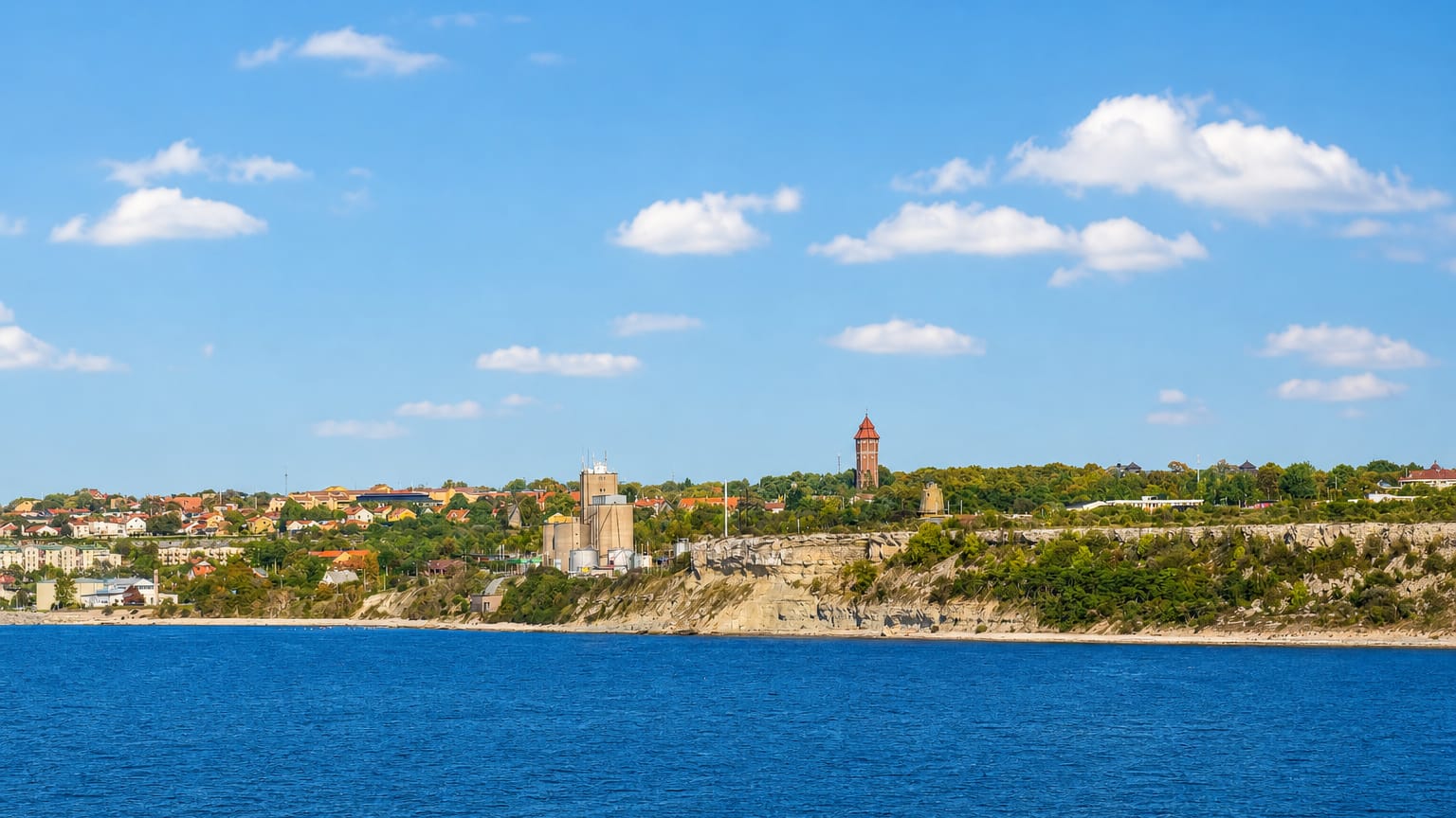 Visby coastline on Gotland, with a red-brick water tower and town rooftops above limestone shore cliffs.