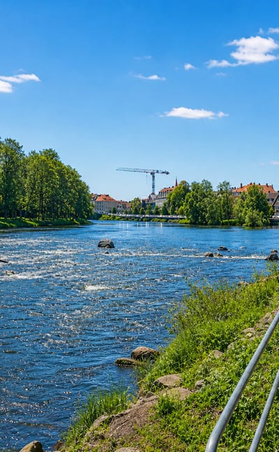The Atran river running through Falkenberg with rapids, a riverside walking path and town buildings beyond