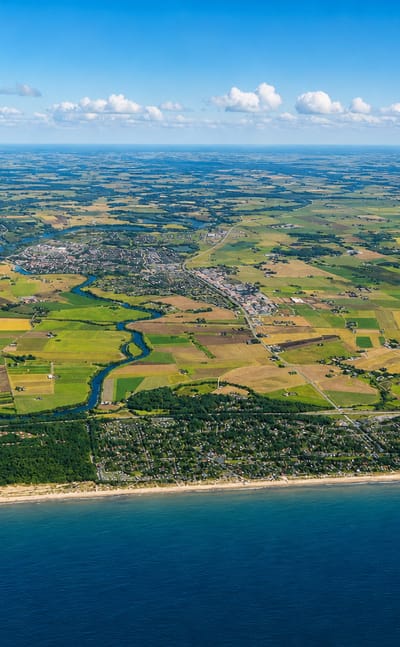 High aerial of the Lagan river winding through farmland to Laholm, Sweden, with the Kattegat coast in the foreground