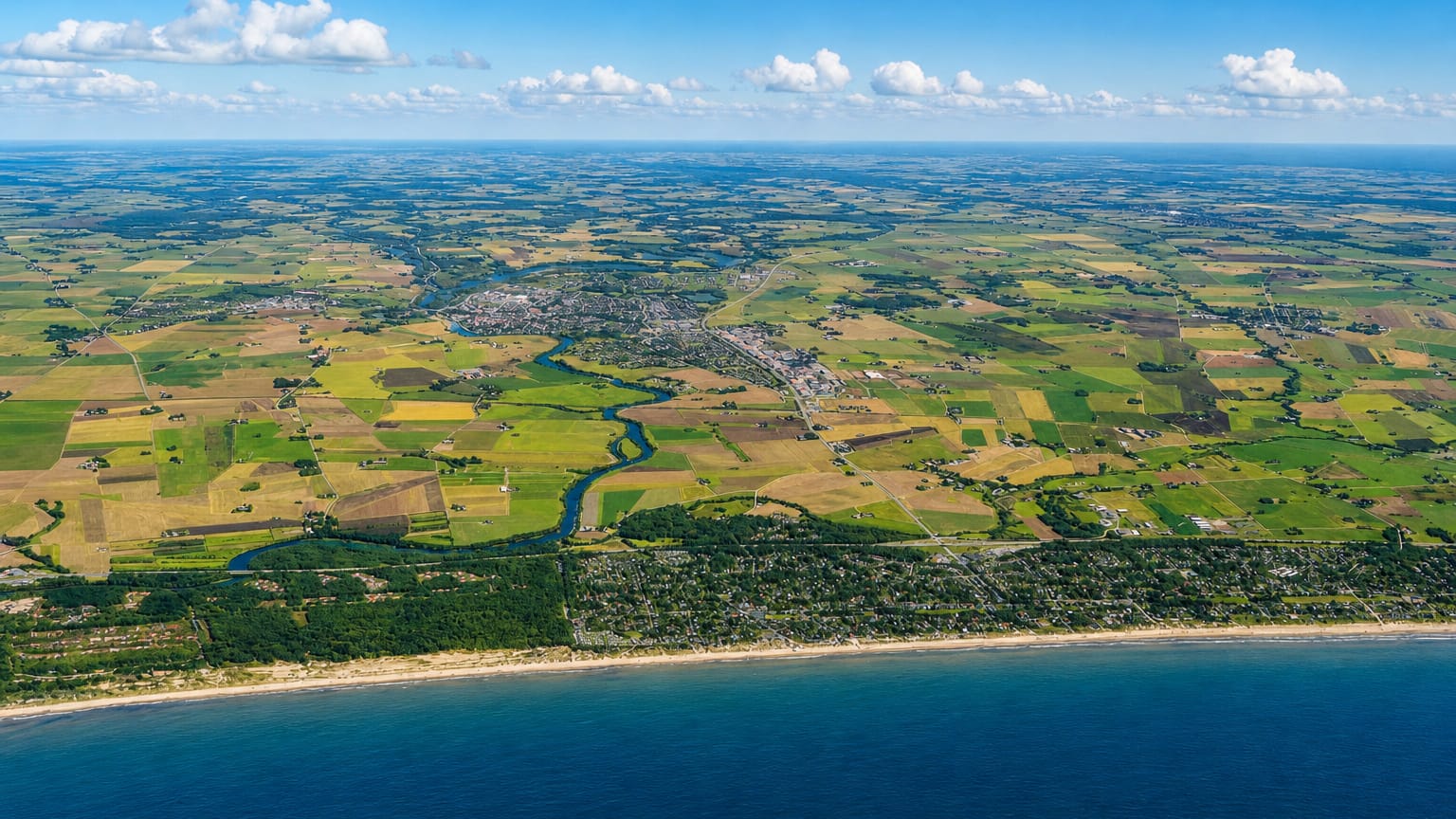 High aerial of the Lagan river winding through farmland to Laholm, Sweden, with the Kattegat coast in the foreground