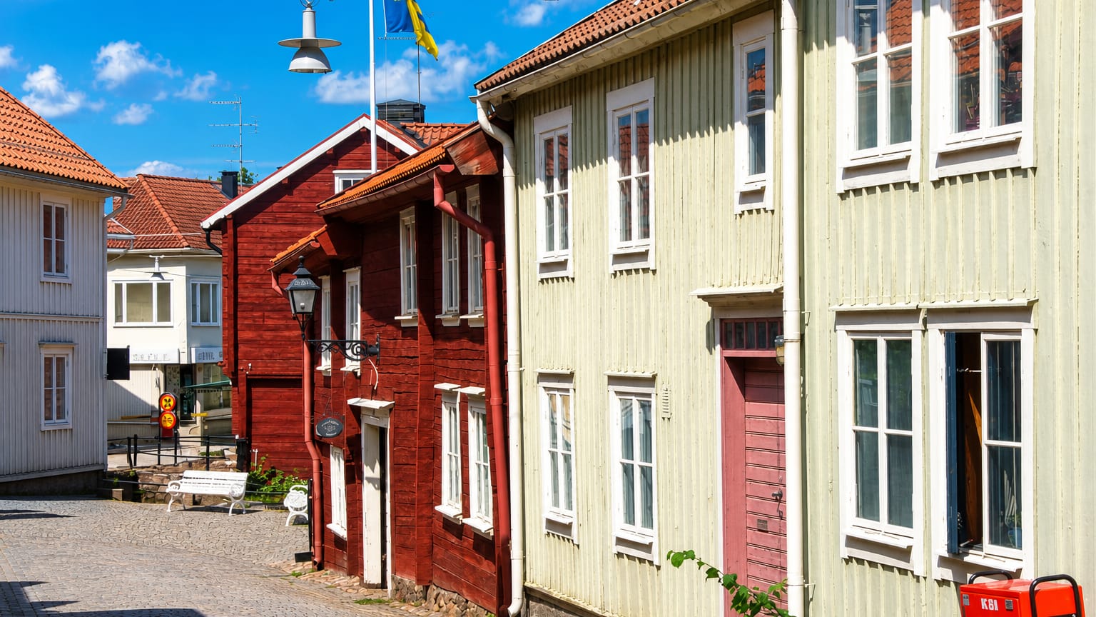 Cobbled lane of red and pale wooden houses in Eksjo's preserved old town with a Swedish flag