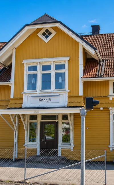 The yellow timber railway station building bearing the Gnosjö nameplate under a blue sky, Sweden.