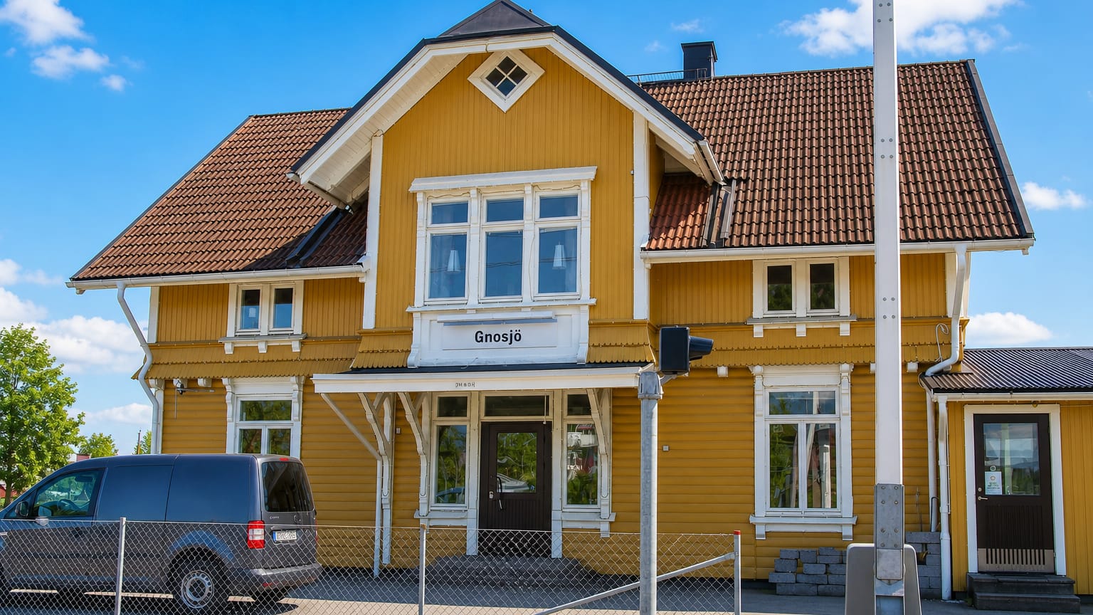 The yellow timber railway station building bearing the Gnosjö nameplate under a blue sky, Sweden.