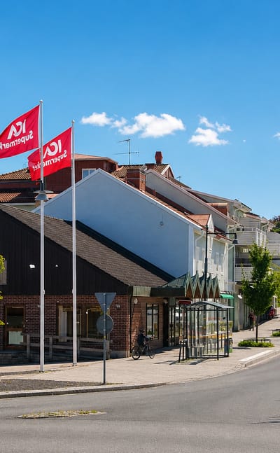 Central street in Habo lined with red ICA supermarket flags, brick buildings and a bus shelter in summer.