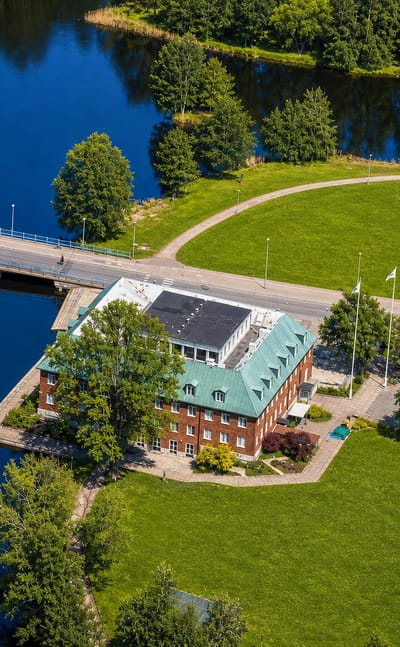 Aerial view of a red-brick green-roofed building beside a lake and road bridge at Tranås, Sweden.