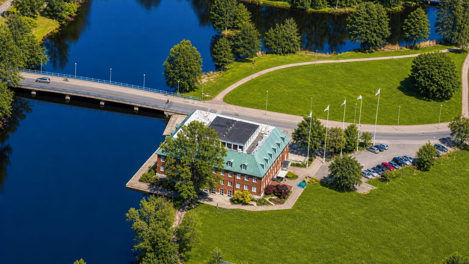 Aerial view of a red-brick green-roofed building beside a lake and road bridge at Tranås, Sweden.