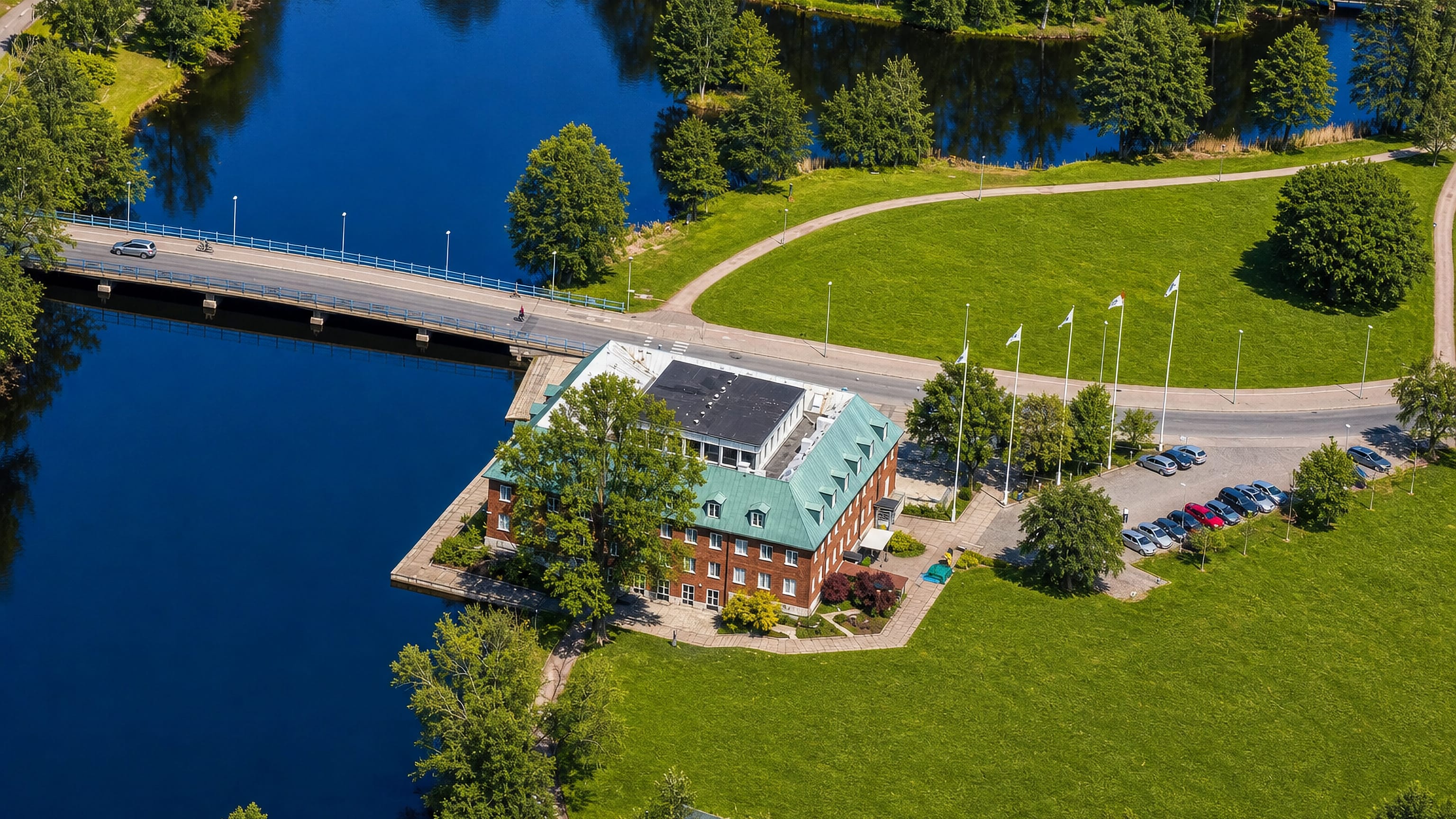 Aerial view of a red-brick green-roofed building beside a lake and road bridge at Tranås, Sweden.