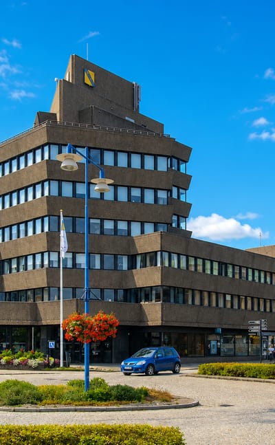 A distinctive stepped brutalist office tower above a roundabout with flowerbeds in Vetlanda, Sweden