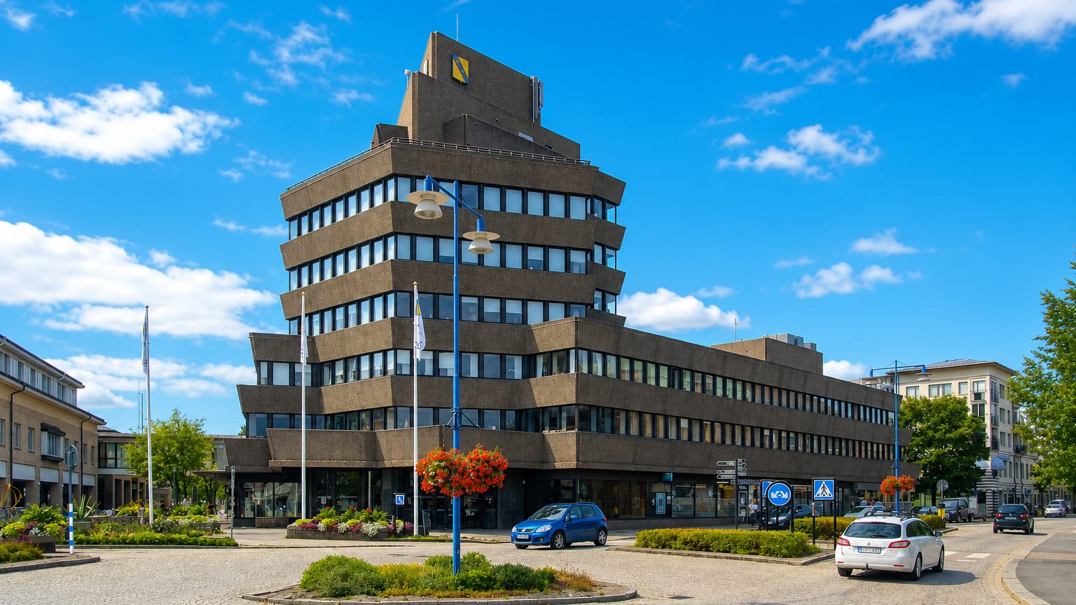 A distinctive stepped brutalist office tower above a roundabout with flowerbeds in Vetlanda, Sweden