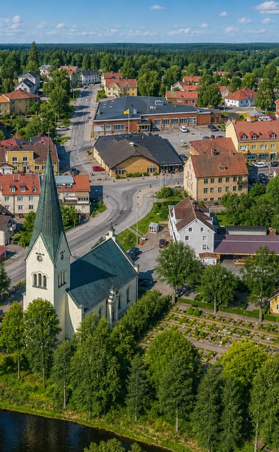 Aerial view of Högsby, Sweden, its green-spired church and red-roofed houses beside the Emån river and a stone bridge.