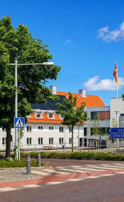 Sunny street in Torsås, Sweden, with white tile-roofed buildings, a flag, and road signs to Kalmar and Söderåkra.