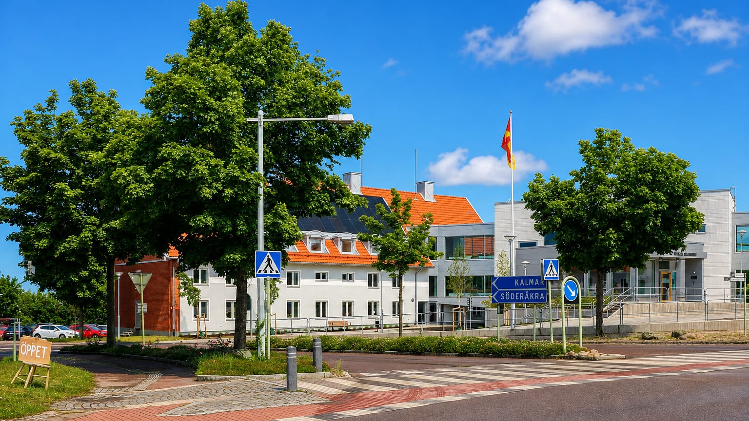 Sunny street in Torsås, Sweden, with white tile-roofed buildings, a flag, and road signs to Kalmar and Söderåkra.
