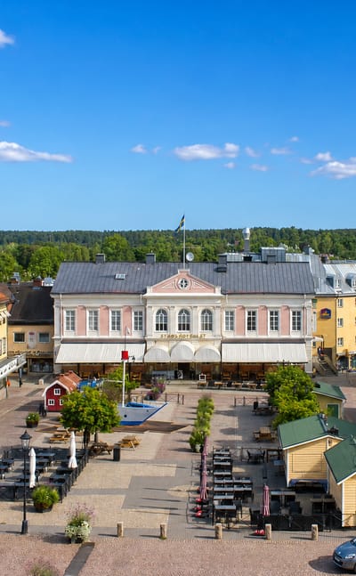 Vimmerby's historic cobbled market square framed by pastel and yellow wooden buildings and cafes under a blue sky.