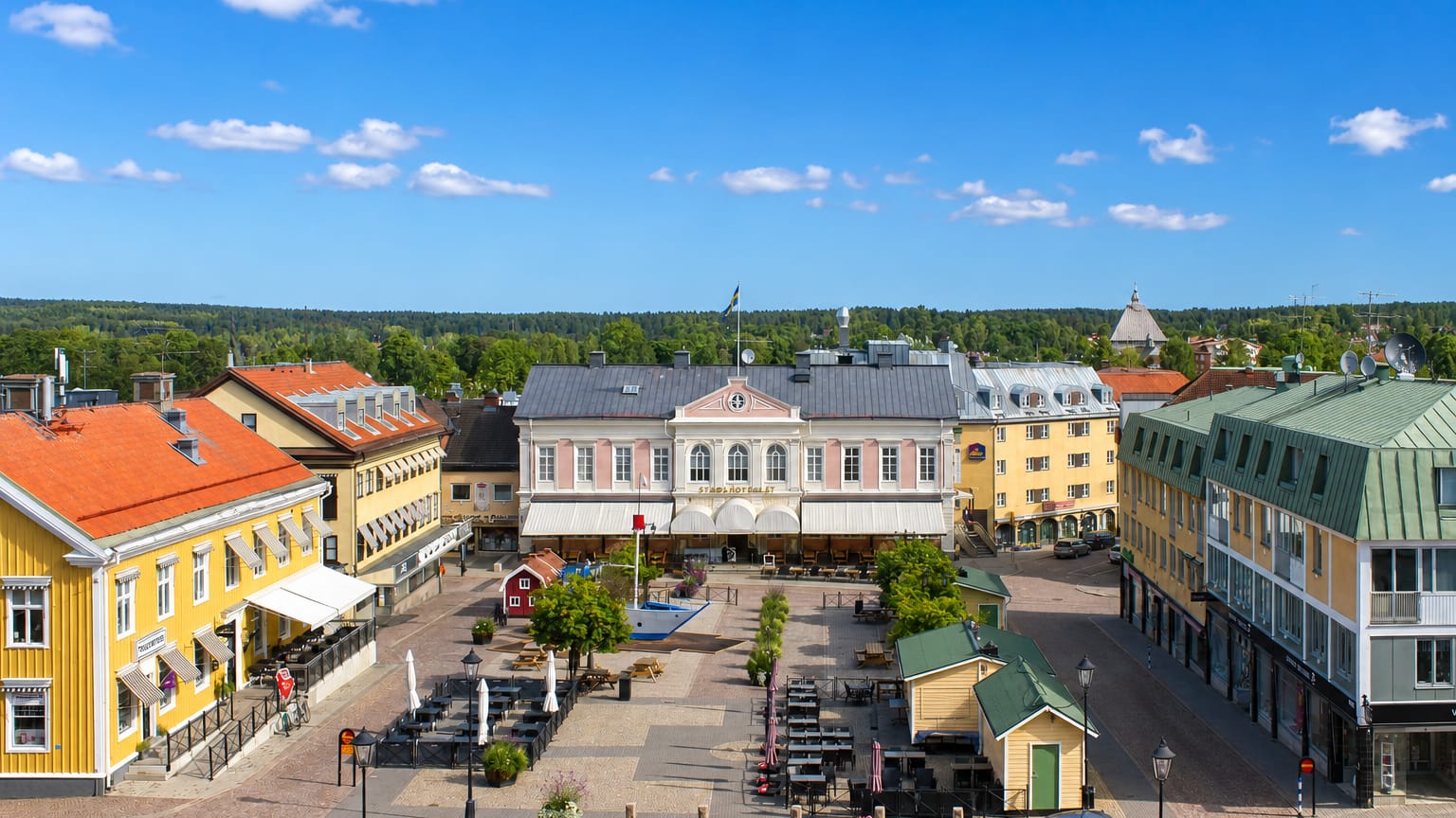 Vimmerby's historic cobbled market square framed by pastel and yellow wooden buildings and cafes under a blue sky.