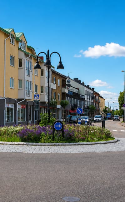 Flower-planted roundabout and town-centre shops with a copper-domed bank in Markaryd, Sweden.