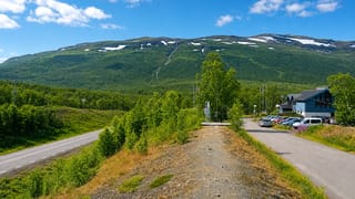 A mountain landscape at Abisko in Swedish Lapland with a road, birch scrub and a modern building below snow-streaked fells.