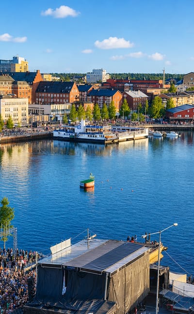 Summer waterfront in Lulea, Sweden, with harbour buildings, boats and a crowd gathered by an event stage