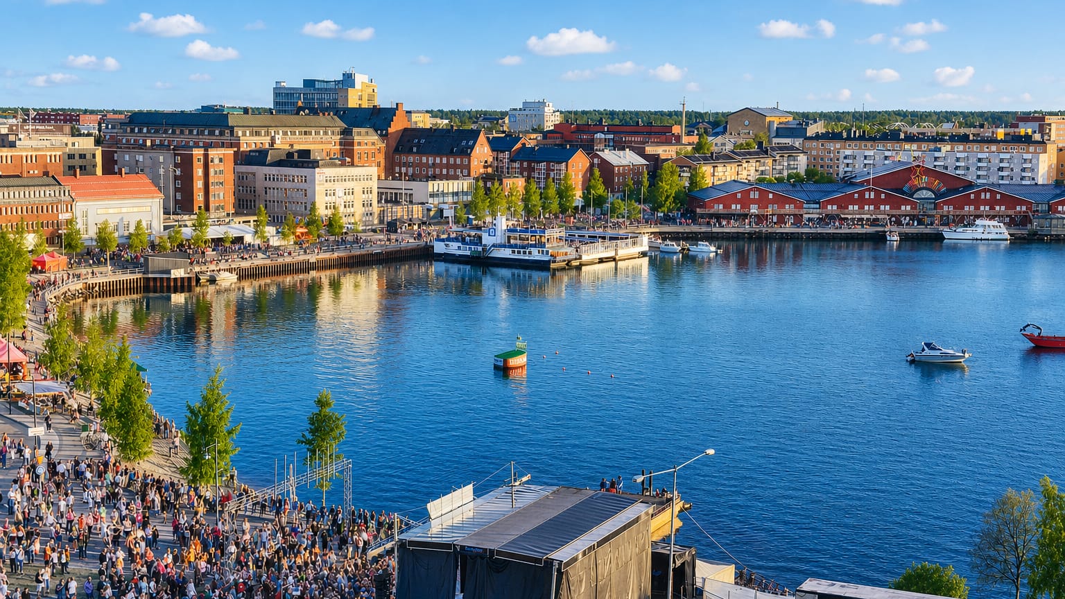 Summer waterfront in Lulea, Sweden, with harbour buildings, boats and a crowd gathered by an event stage