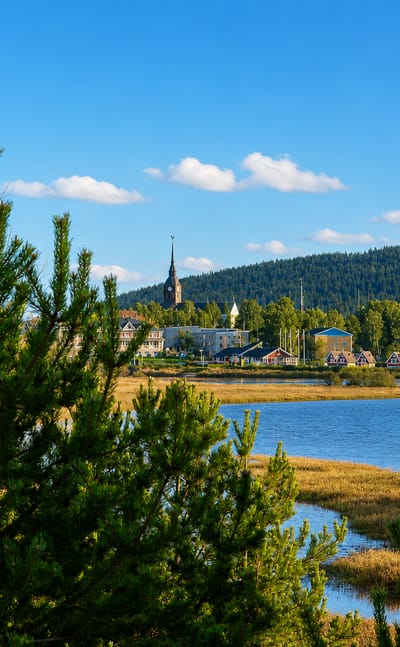 Överkalix, Sweden, a northern town with a church spire across a river and reed beds, framed by pine forest.