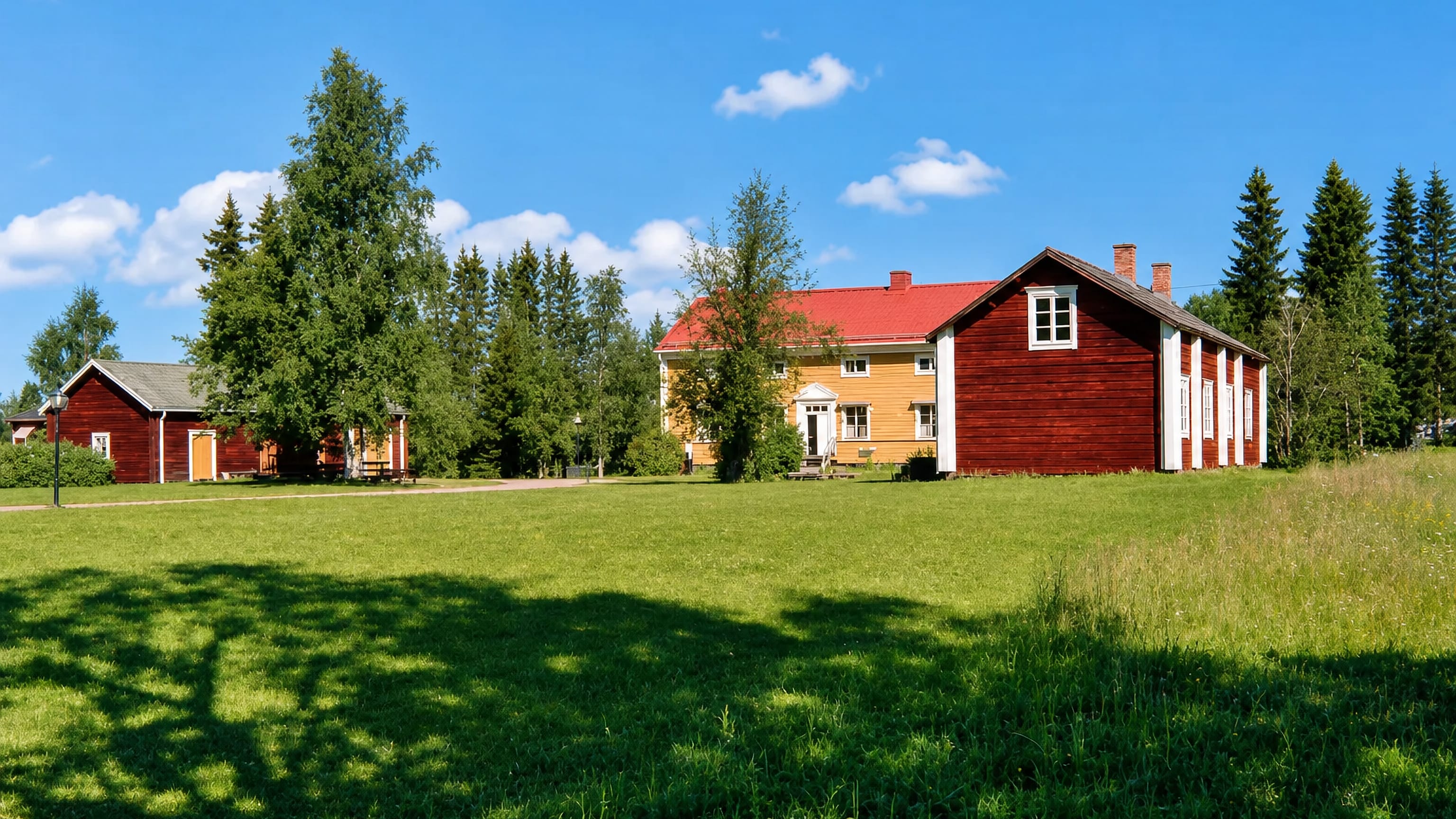 Red timber farm buildings and a yellow manor house beside a summer meadow in Pajala, northern Sweden