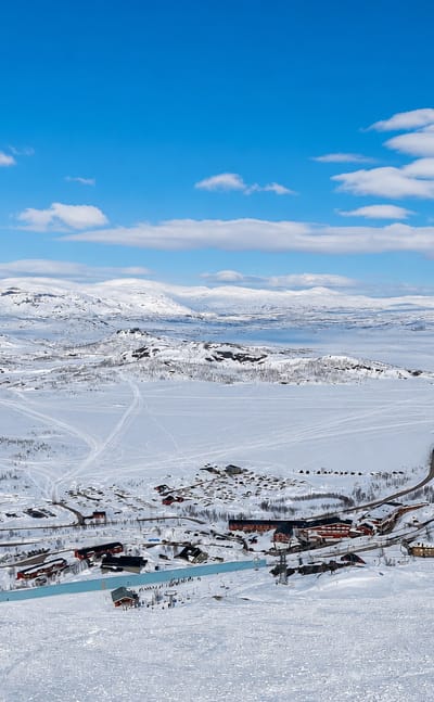 Snow-covered ski resort of Riksgraensen in Swedish Lapland with a cluster of lodges and lifts amid vast white fells.