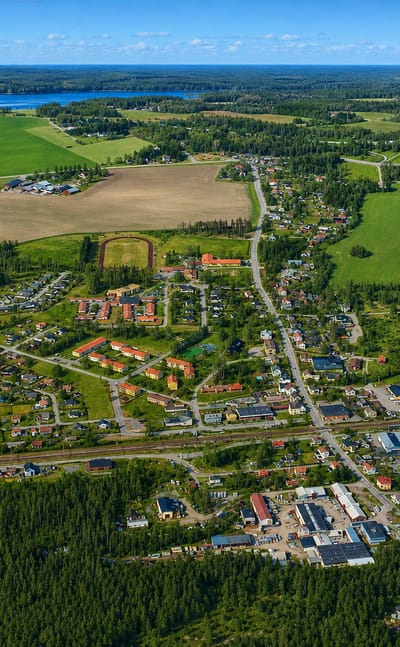 Aerial view of Hallsberg's houses and railway lines set among fields, forest and a distant lake.