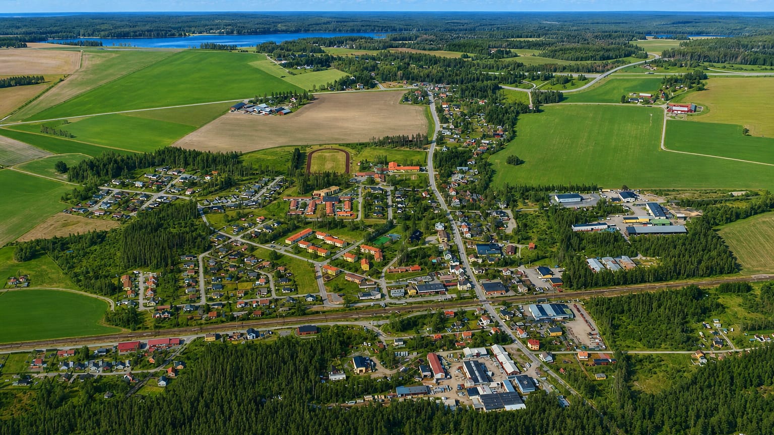 Aerial view of Hallsberg's houses and railway lines set among fields, forest and a distant lake.