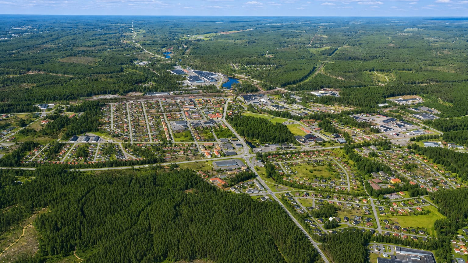 Aerial view of Laxå, a small Swedish town set among extensive pine forest under a blue summer sky.