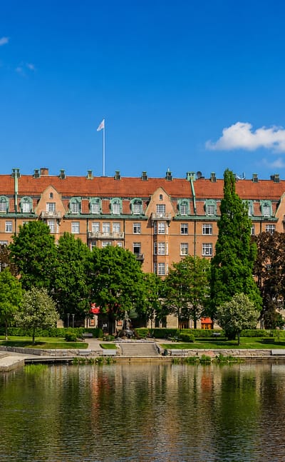 Orebro's red-brick Statt building and the round stone tower of Orebro Castle reflected in the Svartan river on a summer day.