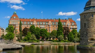 Orebro's red-brick Statt building and the round stone tower of Orebro Castle reflected in the Svartan river on a summer day.