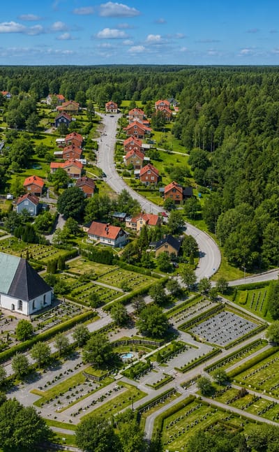 Aerial view of Kisa, Sweden, its white spired church and red-roofed houses beside a large cemetery ringed by forest.