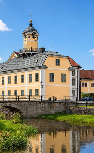 Söderköping's yellow town hall and clock-tower cupola beside the canal and old stone bridge under a summer sky.