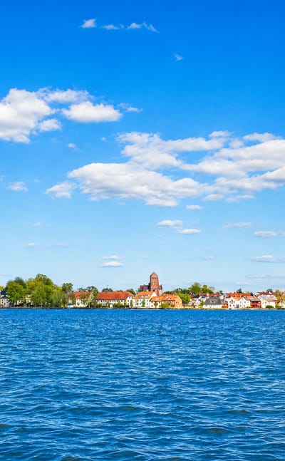 Vadstena's church spire and abbey tower with waterfront houses seen across the blue expanse of Lake Vattern, Sweden.