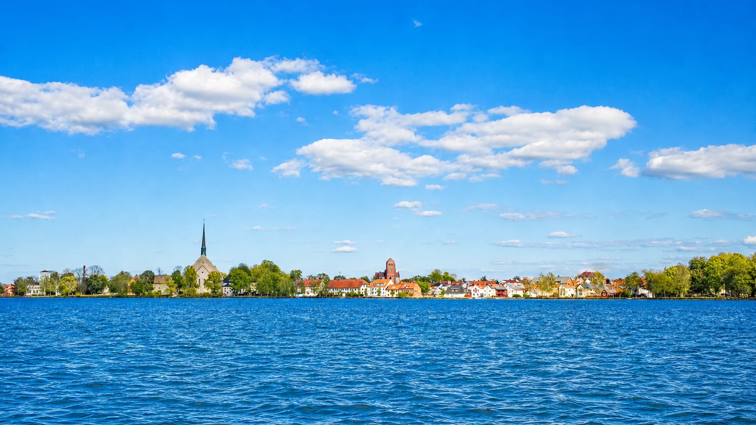 Vadstena's church spire and abbey tower with waterfront houses seen across the blue expanse of Lake Vattern, Sweden.