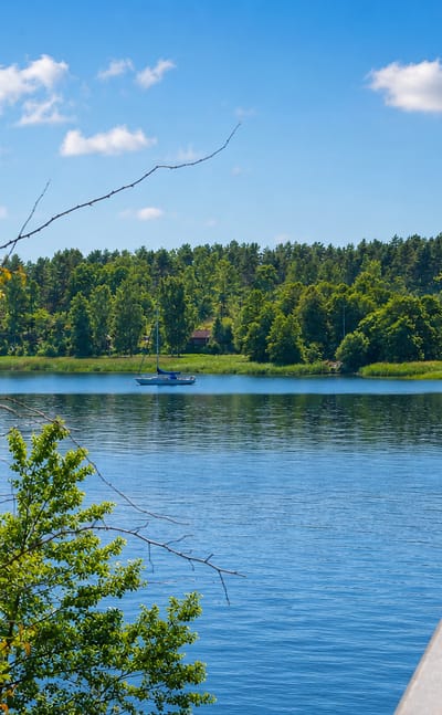 Calm lake with a sailboat and forested shore seen from a bridge at Valdemarsvik, Sweden