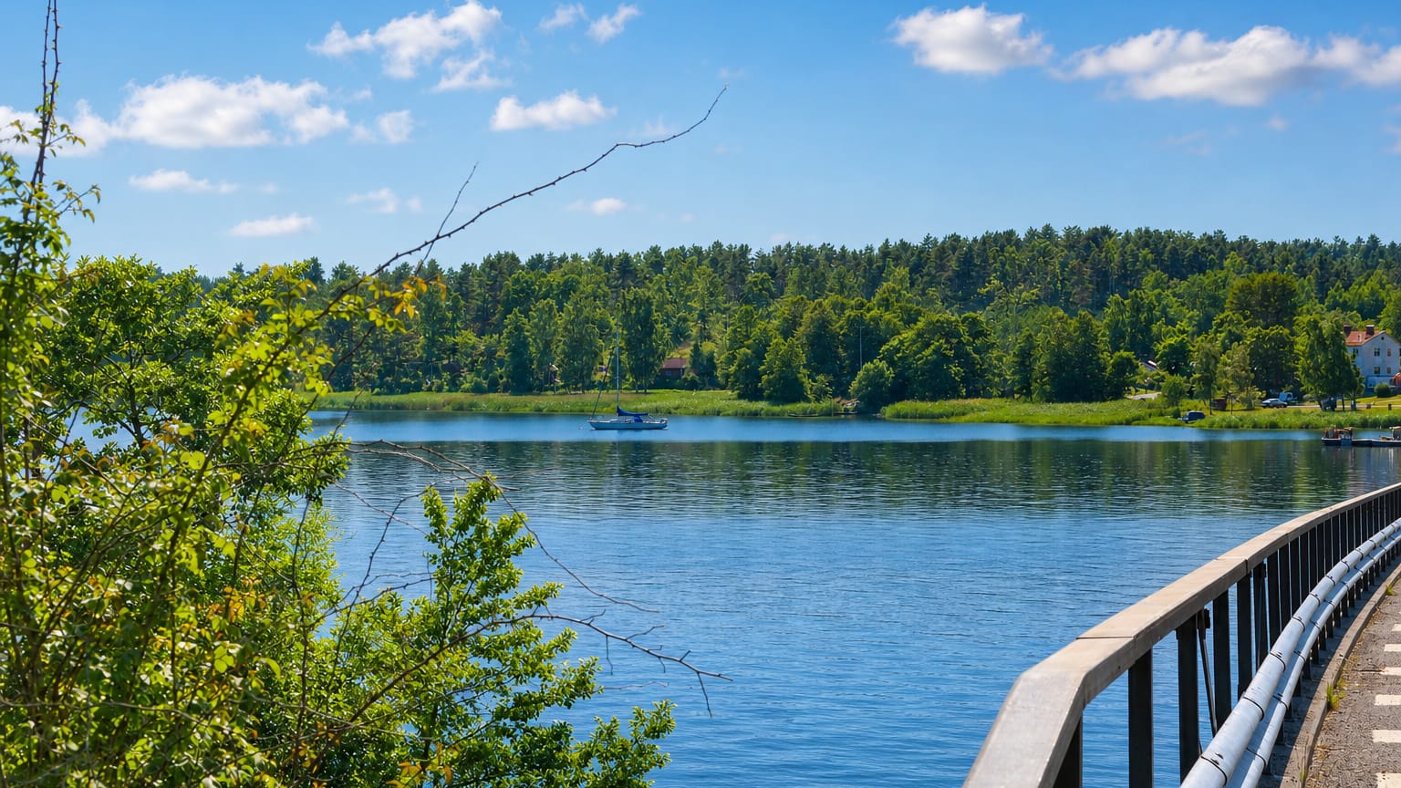 Calm lake with a sailboat and forested shore seen from a bridge at Valdemarsvik, Sweden