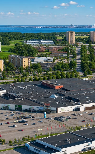 Aerial view of Arlov, Sweden, with a large shopping centre, car parks and apartment blocks, and Malmo across the Oresund beyond.