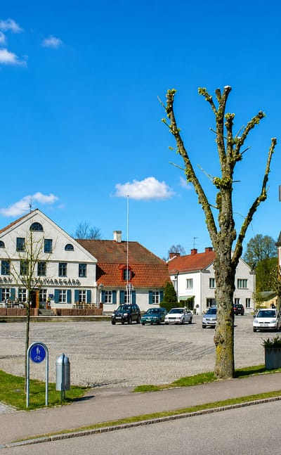 Market square in Broby, Skåne, with a white gabled building, pollarded trees and cobbled paving